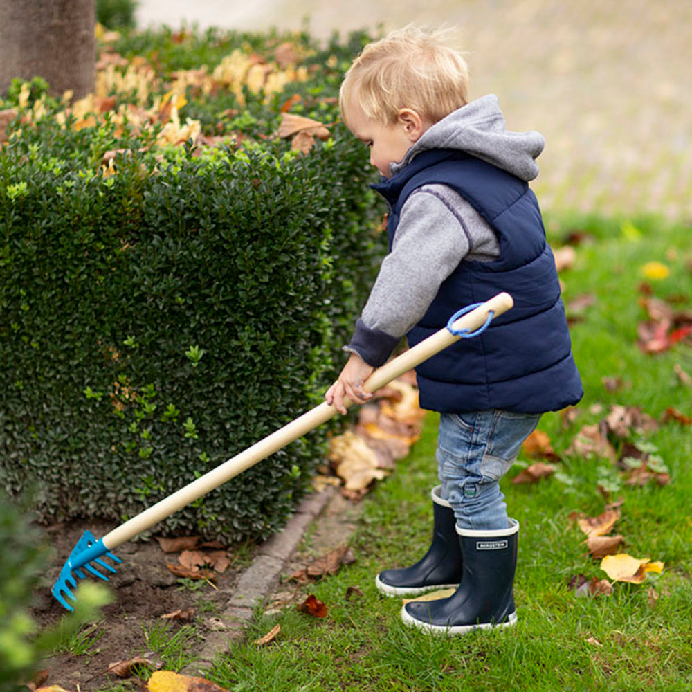 enfant en plein jardinage avec son rateau bleu en metal et en bois 